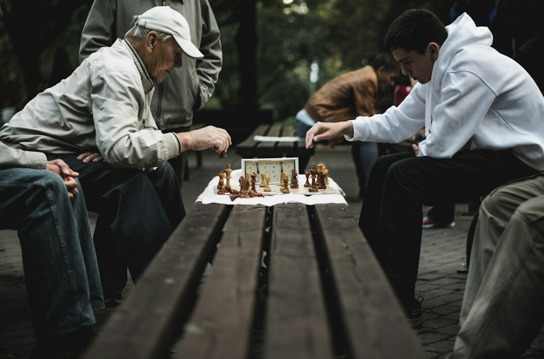 Two elderly men playing chess at a wooden table in a community center